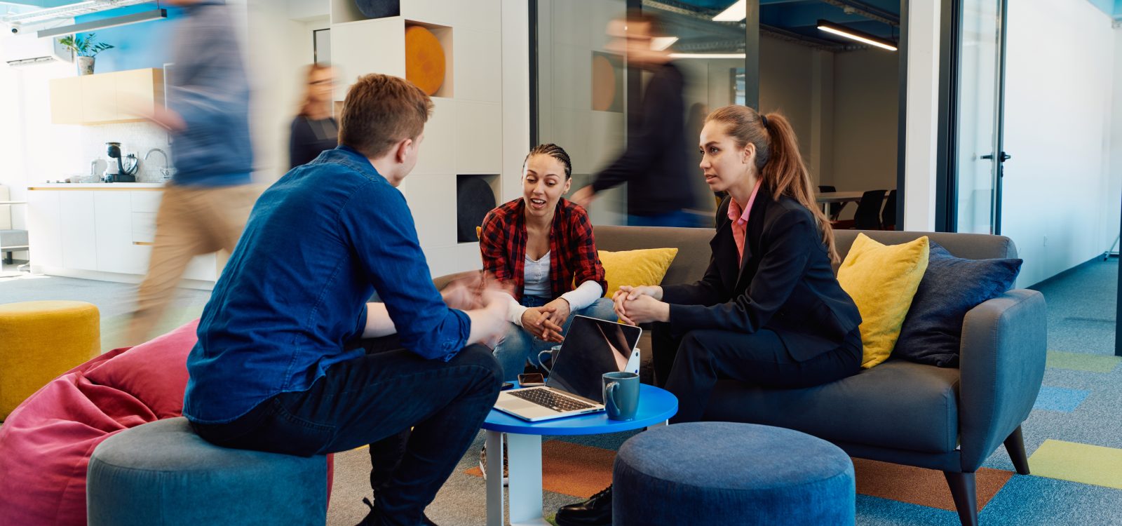 Multiethnic startup business team on meeting in a modern bright open space coworking office. Brainstorming, working on laptop. Group of coworkers walking around in motion blur