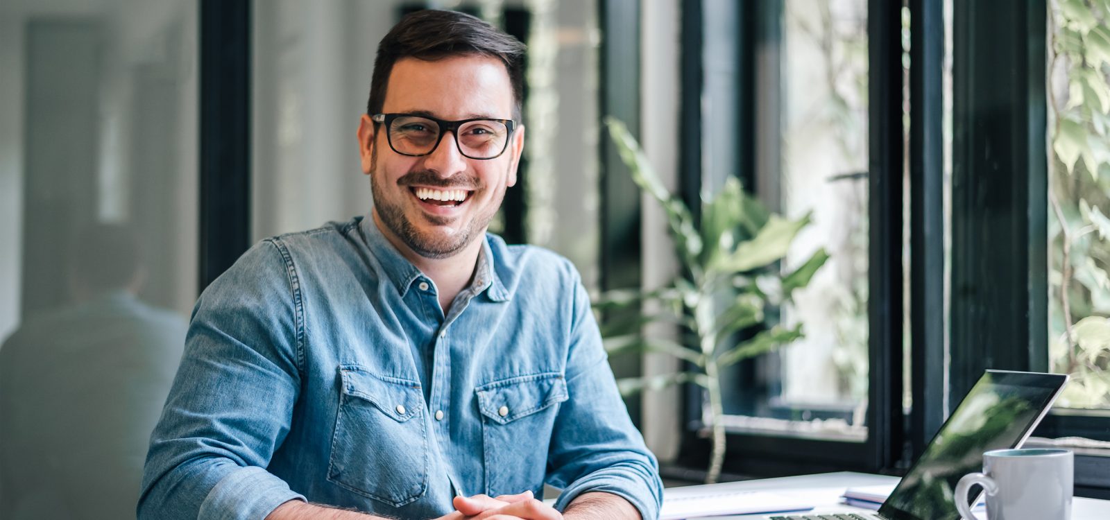 Portrait of young smiling happy handsome successful businessman entrepreneur freelancer working from home office on laptop computer looking at camera