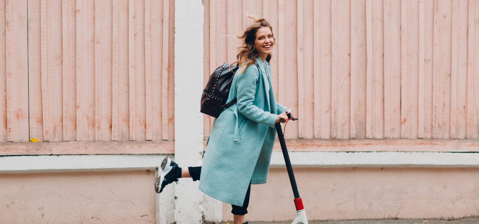 Young woman with electric scooter in blue coat at the city